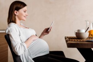 side view of happy pregnant woman using smartphone near tasty breakfast